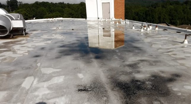 Standing water on a roof with deteriorating roofing membrane and dirt